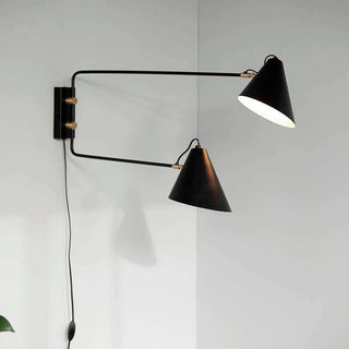 Zwarte dubbele wandlamp met twee conische kappen, goudkleurige details en snoer