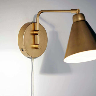 Detail van messing wandlamp Game met ronde wandplaat, armbevestiging, snoer en brandende kap