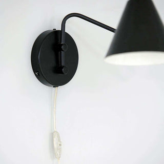 Detail van de zwarte ronde wandplaat en gebogen arm van wandlamp Game met snoer en schakelaar