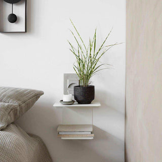 Witte Book wandplank naast een bed, ingericht met een plant, kaars en gestapelde boeken