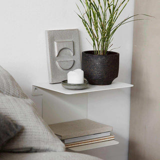 Close-up van de witte Book wandplank naast een bed, met plant, kaars, reliëf en boeken