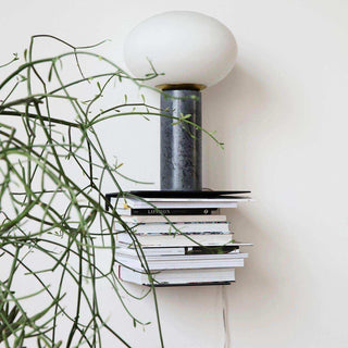 Wandplank Book met een stapel boeken en tafellamp, deels achter groene takken