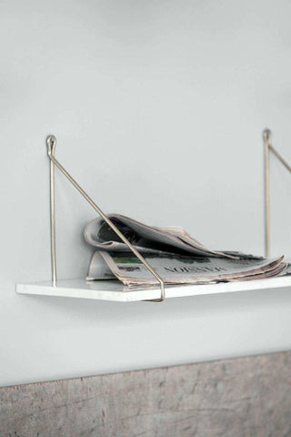 Witte wandplank met metalen houders en opgevouwen kranten erop