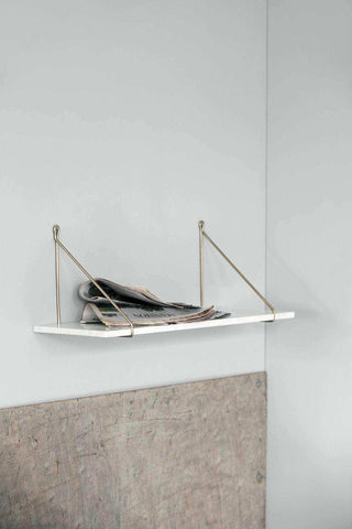 Witte wandplank met gouden metalen ondersteuning en kranten erop