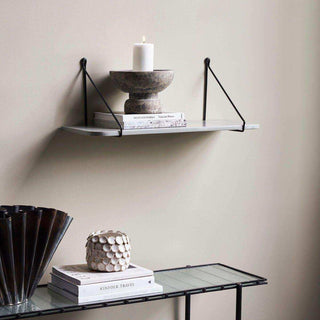 Grijze wandplank Rib aan de muur met zwarte beugels, boeken, schaal en brandende kaars