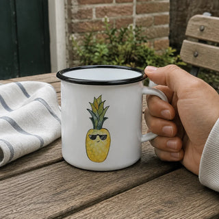 Ligarti emaille mok ananas – 300 ml van dichtbij in gebruik, met de illustratie en dunne zwarte emaille rand zichtbaar.