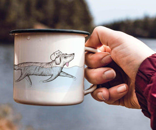 Ligarti emaille mok Badmeester (300 ml) in de hand aan het water, met een illustratie van een hond en een kat op de mok.
