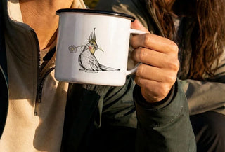 Ligarti emaille mok Bloemenkuif (300 ml) in de hand, in een uitsnede van de gebruiksfoto, met vogel en bloem op de voorkant.