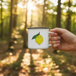 Ligarti emaille mok Citroen (300 ml) in een hand buiten, met gele citroen en groen blad in warm boslicht.