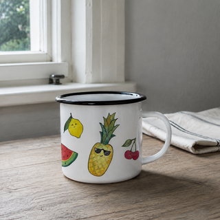Ligarti emaille mok Fruit 300 ml met fruitillustraties op een houten keukentafel bij het raam.