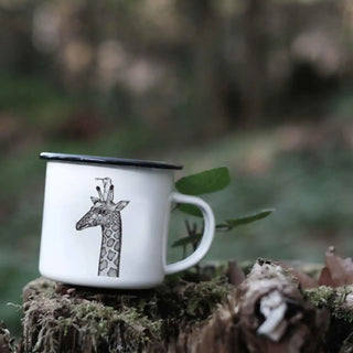 Emaille mok met girafillustratie op een bemoste boomstronk in het bos