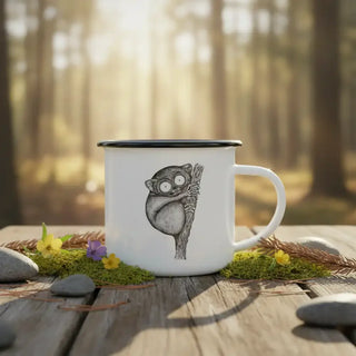 Witte emaille mok met zwarte rand en koboldmaki op een houten ondergrond in het bos