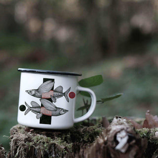 Emaille mok met twee vliegende vissen op een bemoste boomstronk in het bos