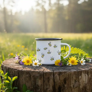 Witte mok met bijenillustraties op een boomstronk tussen gele en witte bloemen