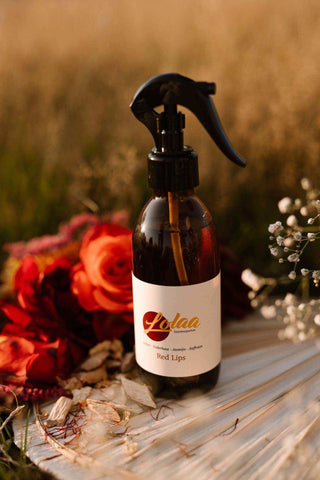 Lolaa Red Lips interieurparfum in bruine fles met zwarte spraykop, omringd door droogbloemen op houten oppervlak