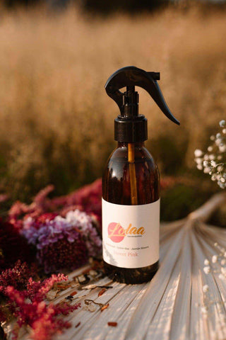 Lolaa Sweet Pink interieurparfum in bruine fles met zwarte spuitdop, omringd door gedroogde bloemen
