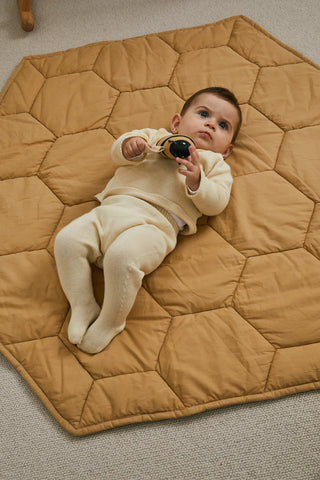 Een baby ligt op de honingkleurige Honey-speelmat.