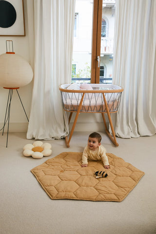 Een baby speelt op de Honey-speelmat bij een wieg.