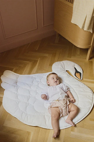 Baby op een ivoorkleurige zwaanspeelmat op de vloer.