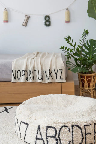 ABC-babydeken met zwarte letters over de rand van een bed.