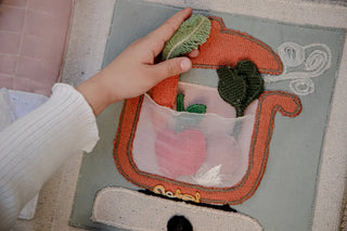 Hand met een stoffen wortel bij het geopende Cool Kids Eat Healthy boek.
