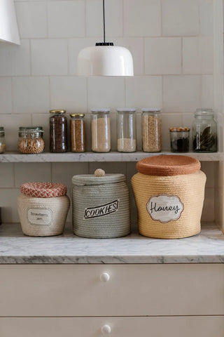 Cookie Jar-, Honey Pot- en Jam Jar-manden naast elkaar op een aanrecht.