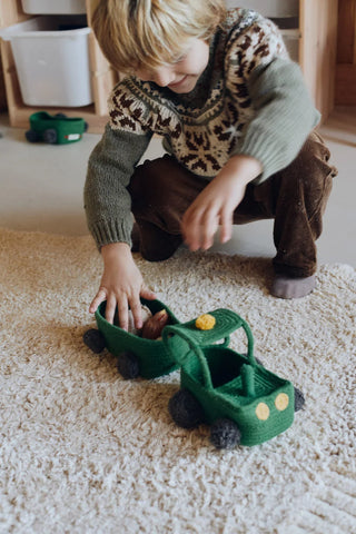 Kind speelt met een groene tractormand en aanhanger.