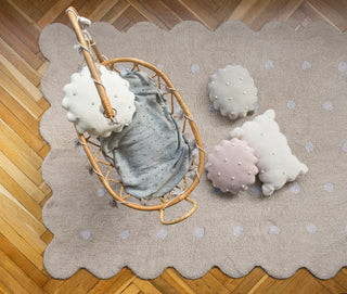 Beige Biscuit-vloerkleed met witte stippen en golvende rand onder een rotan stoel.