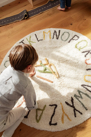 Kind speelt met losse letters op een rond alfabetvloerkleed.
