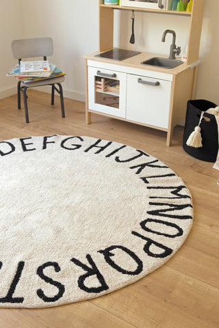 ABC-vloerkleed in naturel met zwarte letters bij een houten speelkeuken.