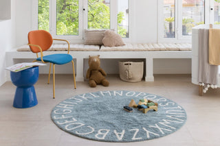Vintageblauw ABC-vloerkleed met houten speelgoed in een lichte kamer.