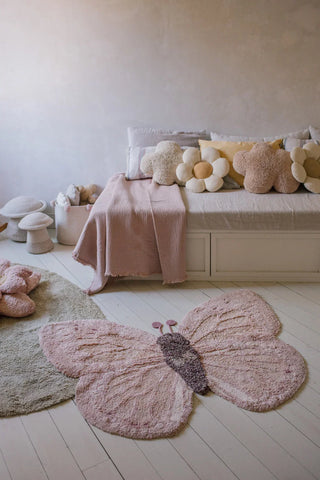 Roze Babut-vloerkleed in vlindervorm voor een bed met bloemkussens.