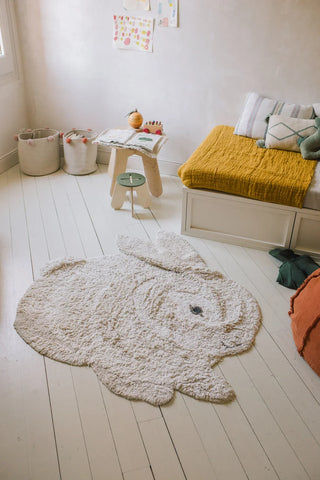 Bunny-vloerkleed in konijnvorm op een lichte vloer naast een bed.
