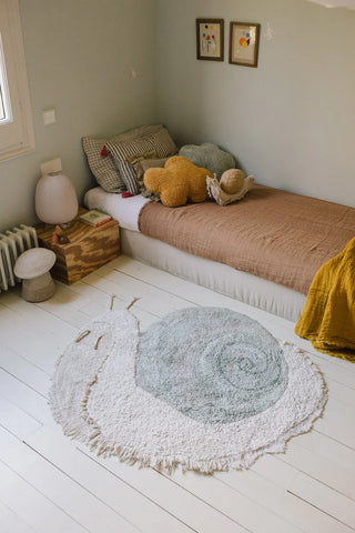 Snail-vloerkleed met blauwgroen huis op de vloer naast een bed.