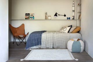 Naturel Bloom-vloerkleed met hoekkwasten naast een bed.