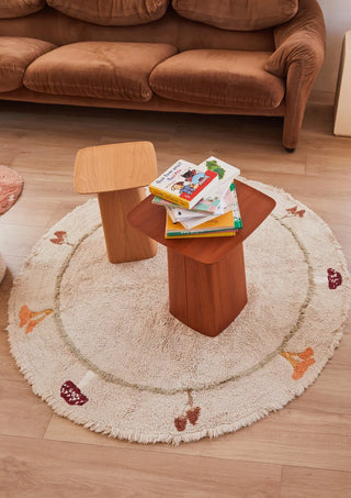 Rond naturel paddenstoelenvloerkleed onder tafeltjes bij een bank.