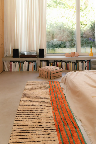 Oranje gestreepte Color On-loper naast een bed.