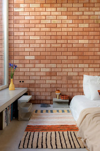 Compact Color On-vloerkleed in warme kleuren naast een bed.