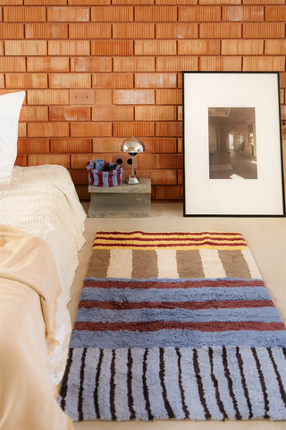 Compact blauw Color On-vloerkleed naast een bed.