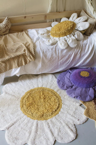 Wit bloemvloerkleed voor een bed met bloemkussens.