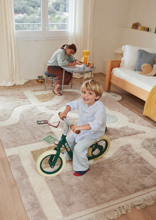 Kind op een fiets op een speelvloerkleed met wegen.