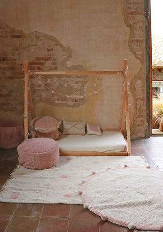 Vloerkleed met roze stippen bij een bed.