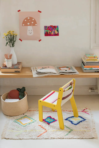 Mini Kaarol-vloerkleed met drie gekleurde ruiten bij een gele kinderstoel.
