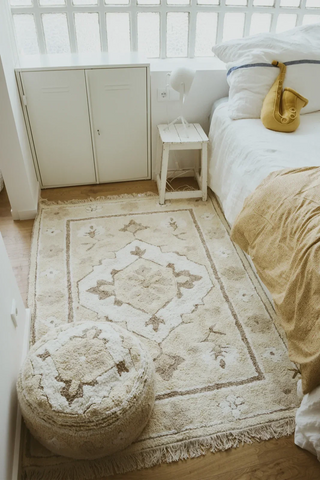 Licht Persian-vloerkleed naast een bed en een ronde poef.