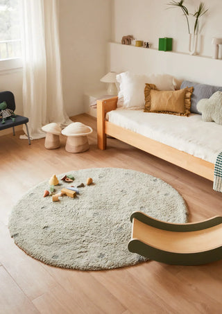 Rond blauwgroen gestippeld vloerkleed bij een bed en stoel.