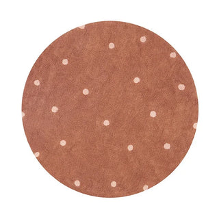 Rond kastanjekleurig vloerkleed met roze stippen.
