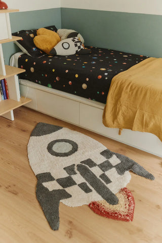 Raketvloerkleed naast een kinderbed.