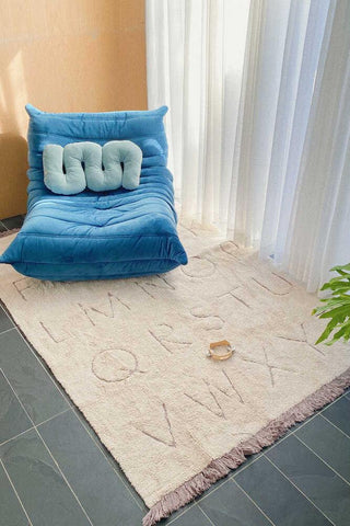 Rugcycled ABC vloerkleed naast een blauwe zitpoef