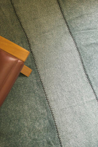 Detail van groen Stoashed-vloerkleed met donkere naden bij een stoel.