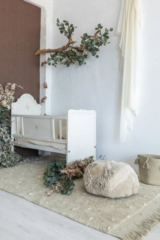 Groen vloerkleed met bosmotieven bij een babybed.